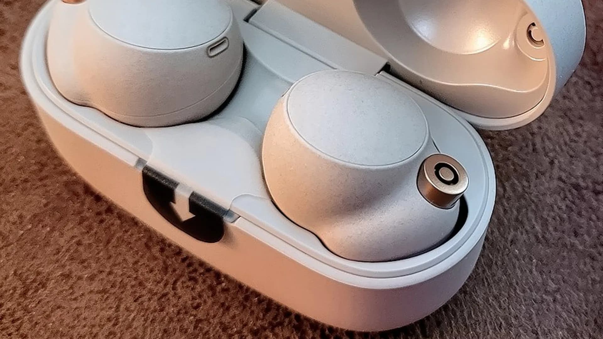 Several pairs of true wireless earbuds in their charging cases arranged on a wooden desk