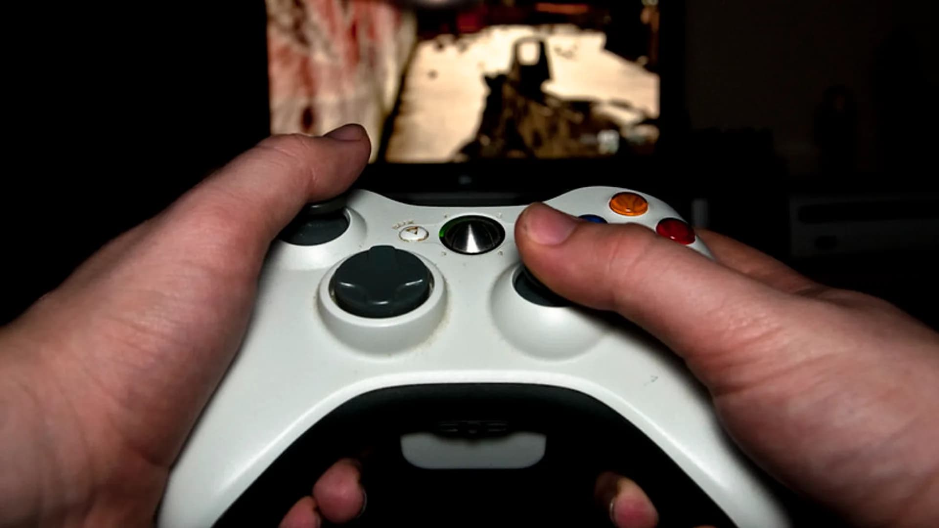 A wireless game controller resting in front of a large TV streaming a video game in a living room