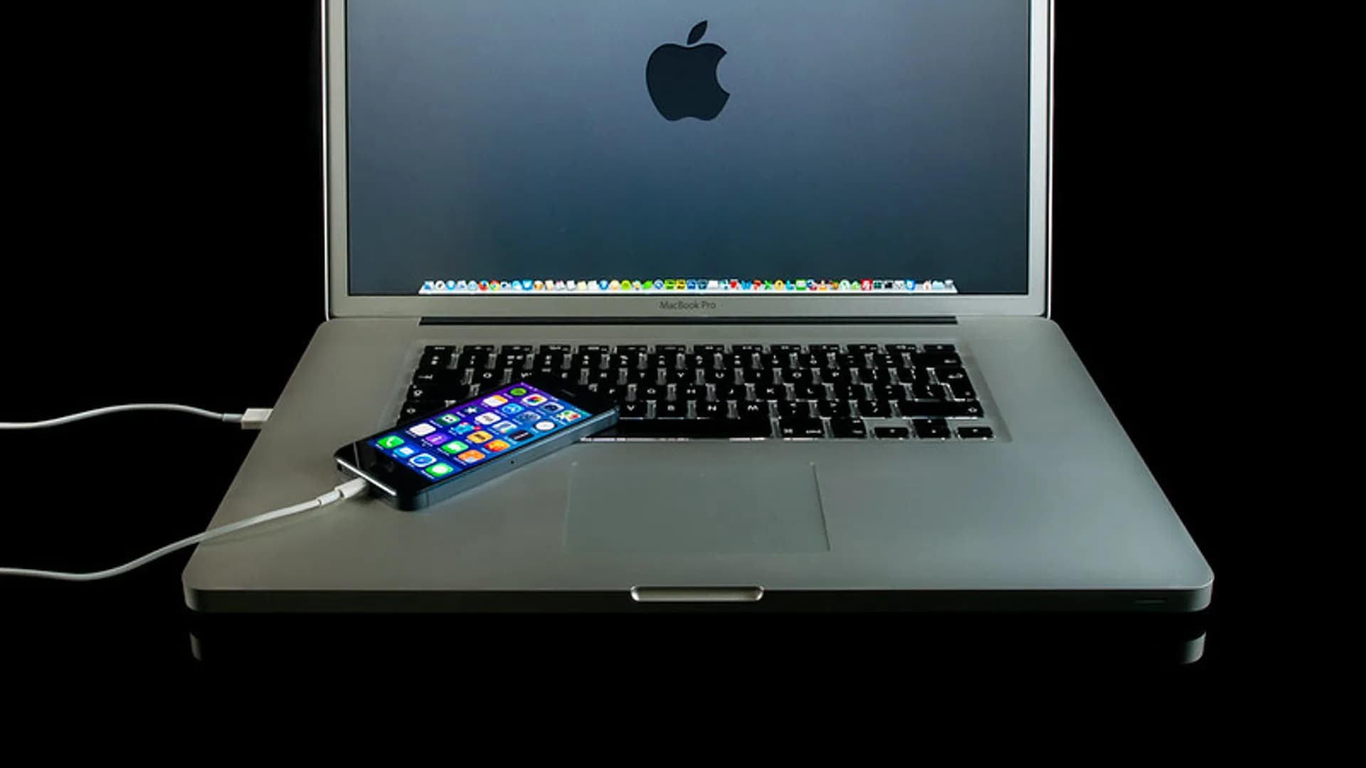 A laptop sitting on a wooden desk with its charging cable plugged in and the battery indicator on screen